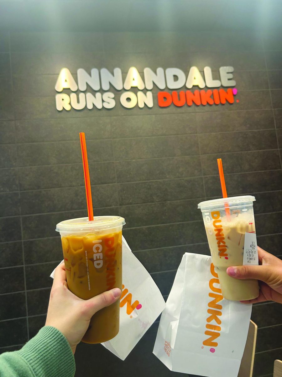 Juniors Zoe Ligairi and Cole Cardwell hold their fall-special drinks and donuts in front of the “Annandale Runs on Dunkin'” sign.