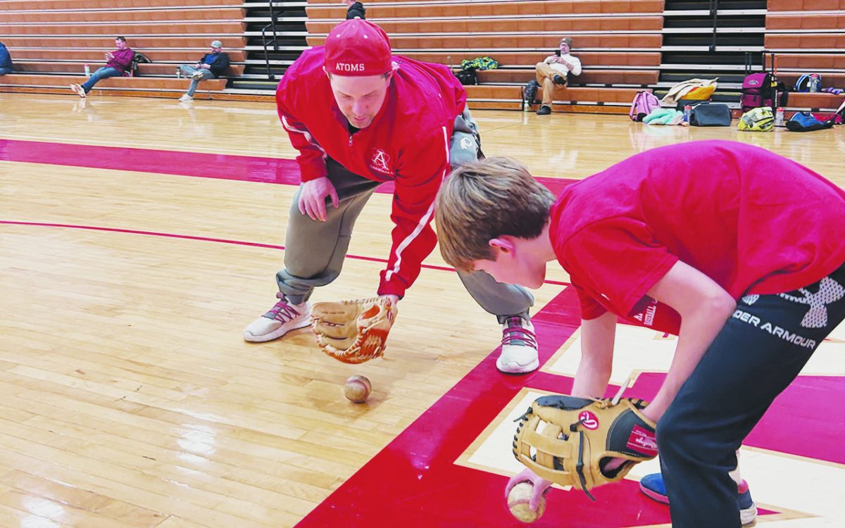 Assistant AHS baseball coach Christopher Bagot runs through a basic fielding drill with an older participant of the camp in the main gym during the 1/19 session. 